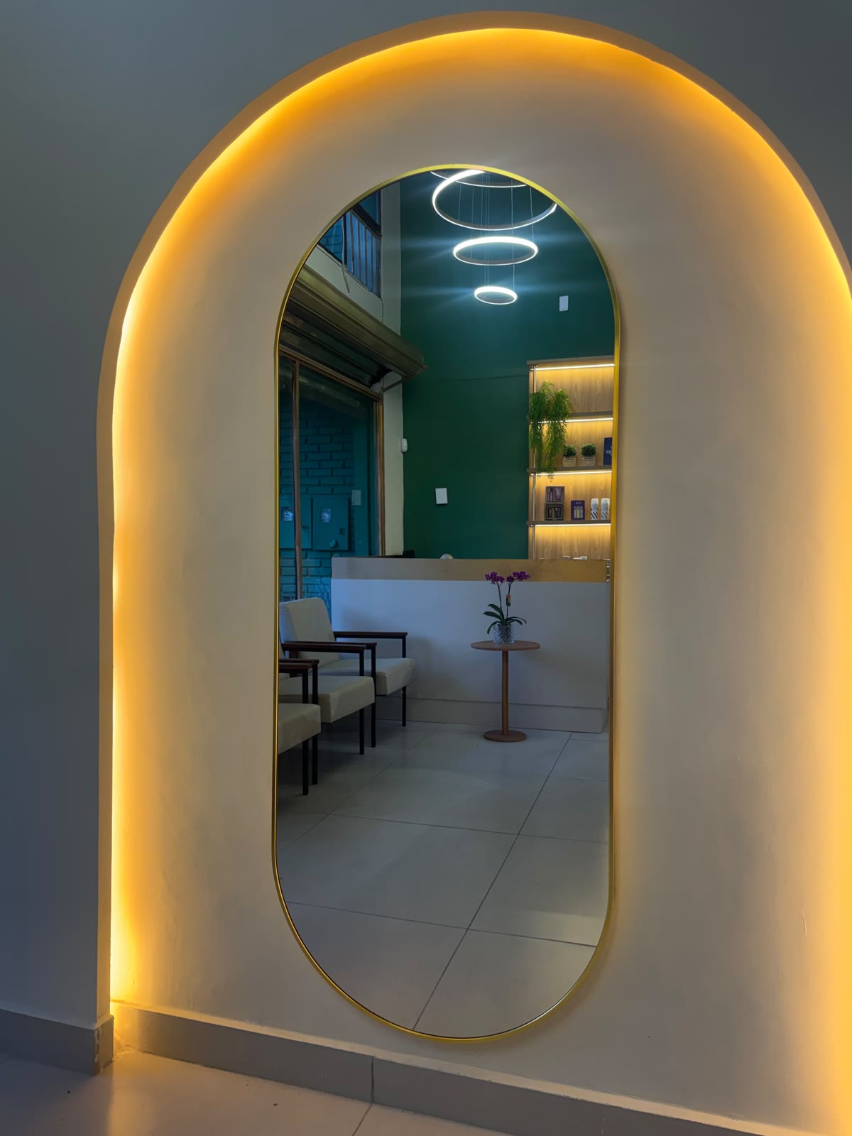 Espelho oval com moldura dourada em arco iluminado, refletindo a recepção da Áurea em Resende